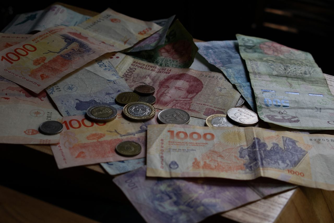A collection of Argentine banknotes and coins displayed on a wooden table.